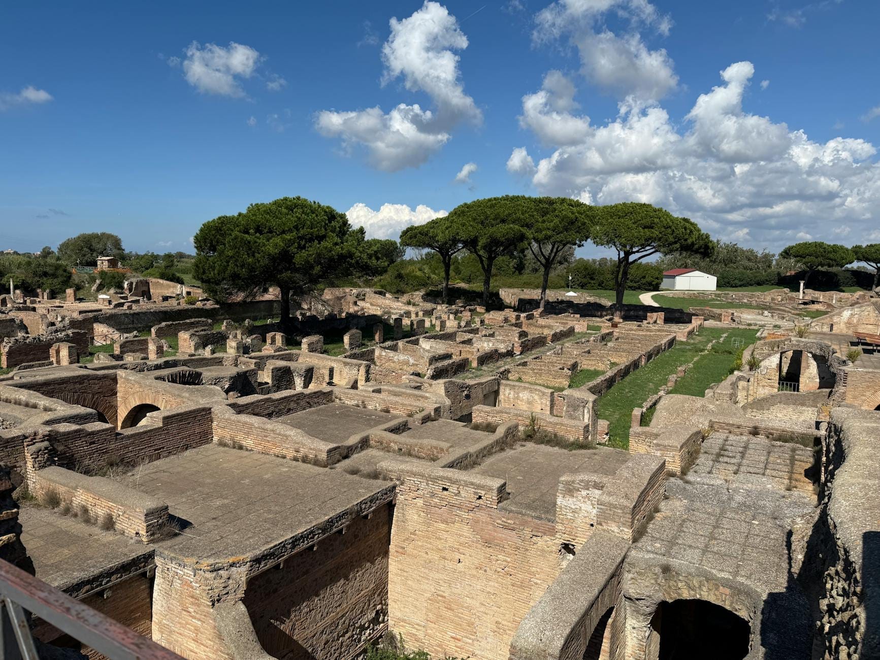 Extensive ancient Roman brick ruins with pine trees, archways, and a blue sky with scattered clouds in Ostia Antica near Rome.