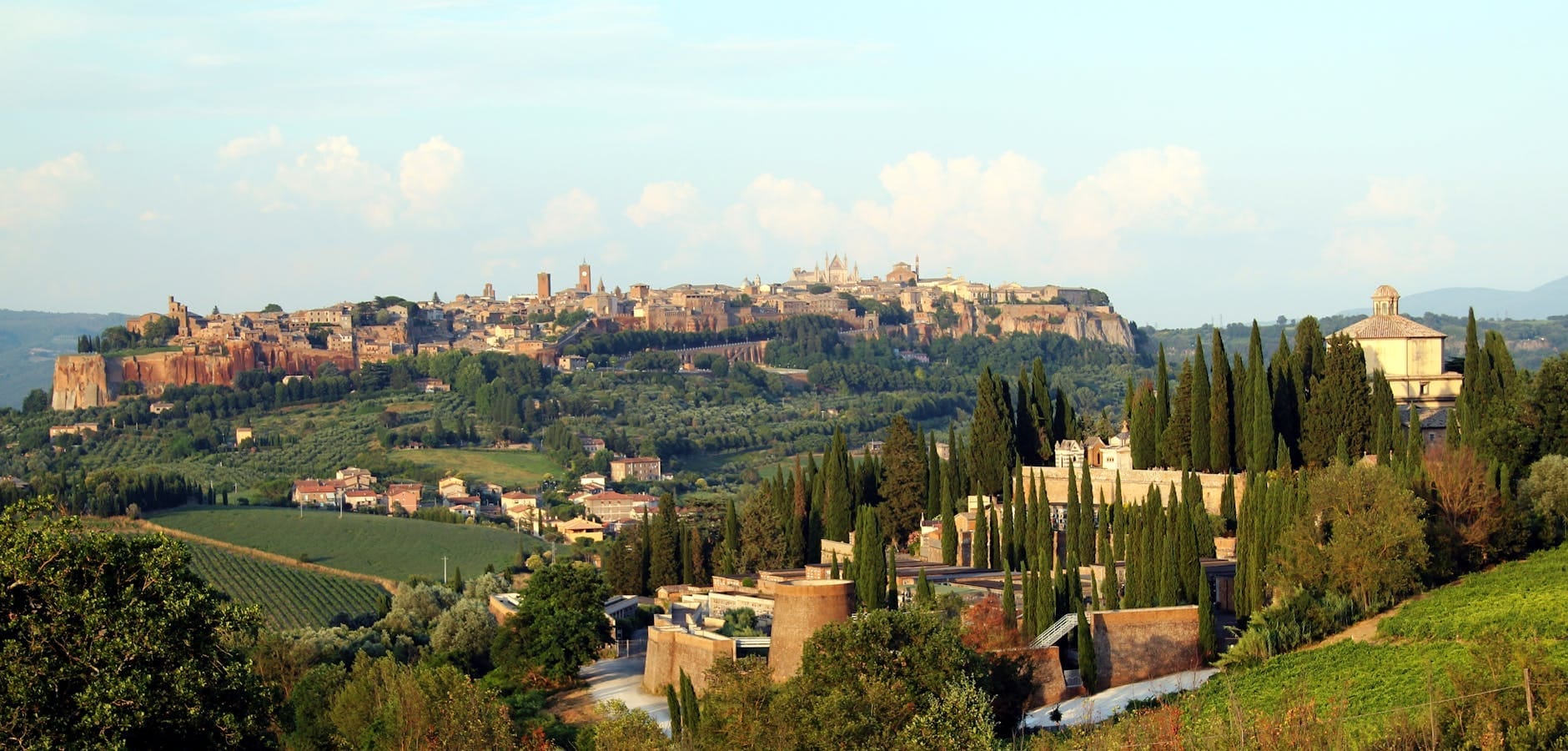 Panoramic view of Orvieto, an Etruscan hill town, perched on a plateau with lush countryside and cypress trees in the foreground.