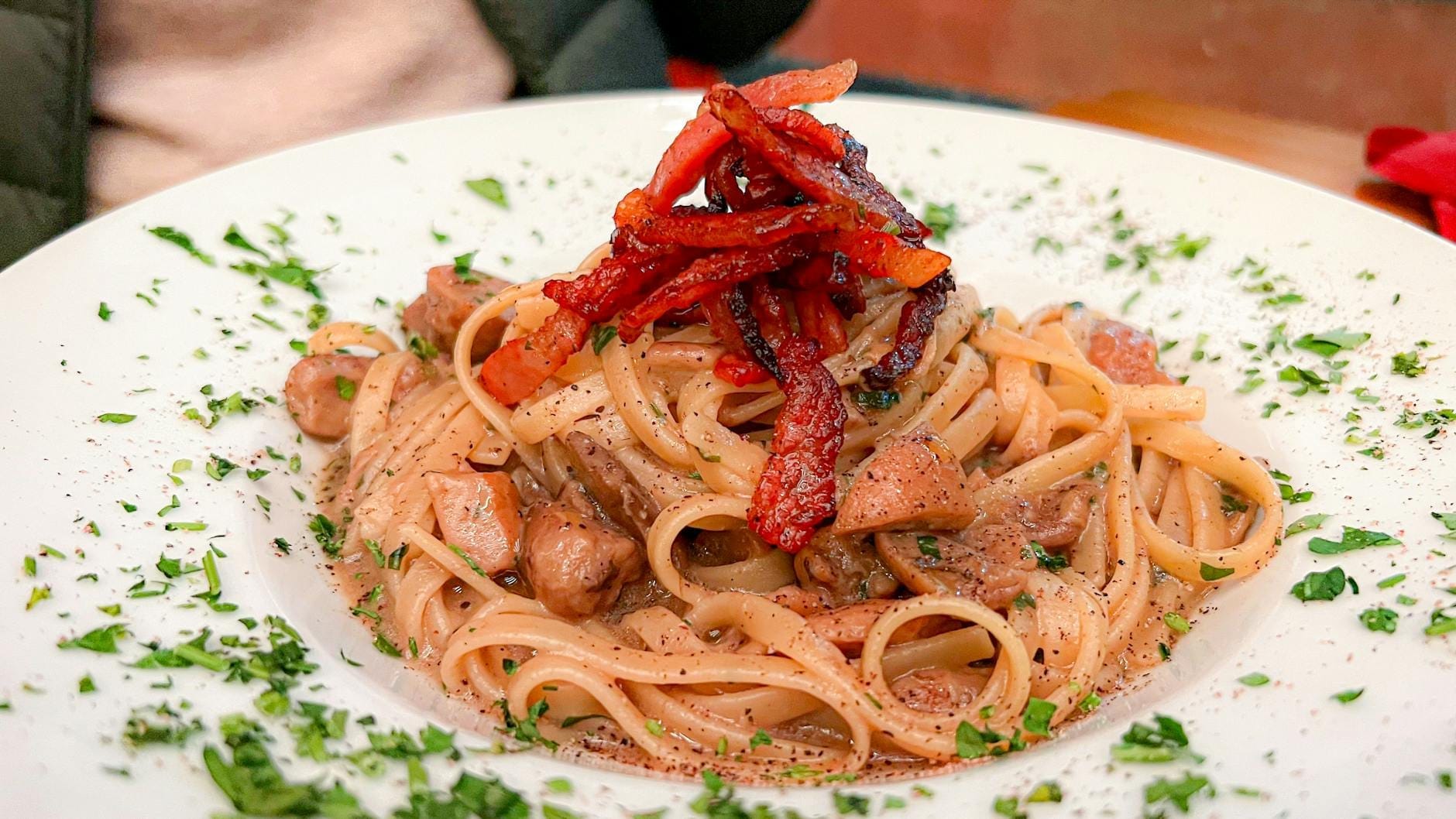 A plate of pasta with guanciale and parsley, likely a Roman dish such as carbonara or amatriciana, served at an outdoor table.