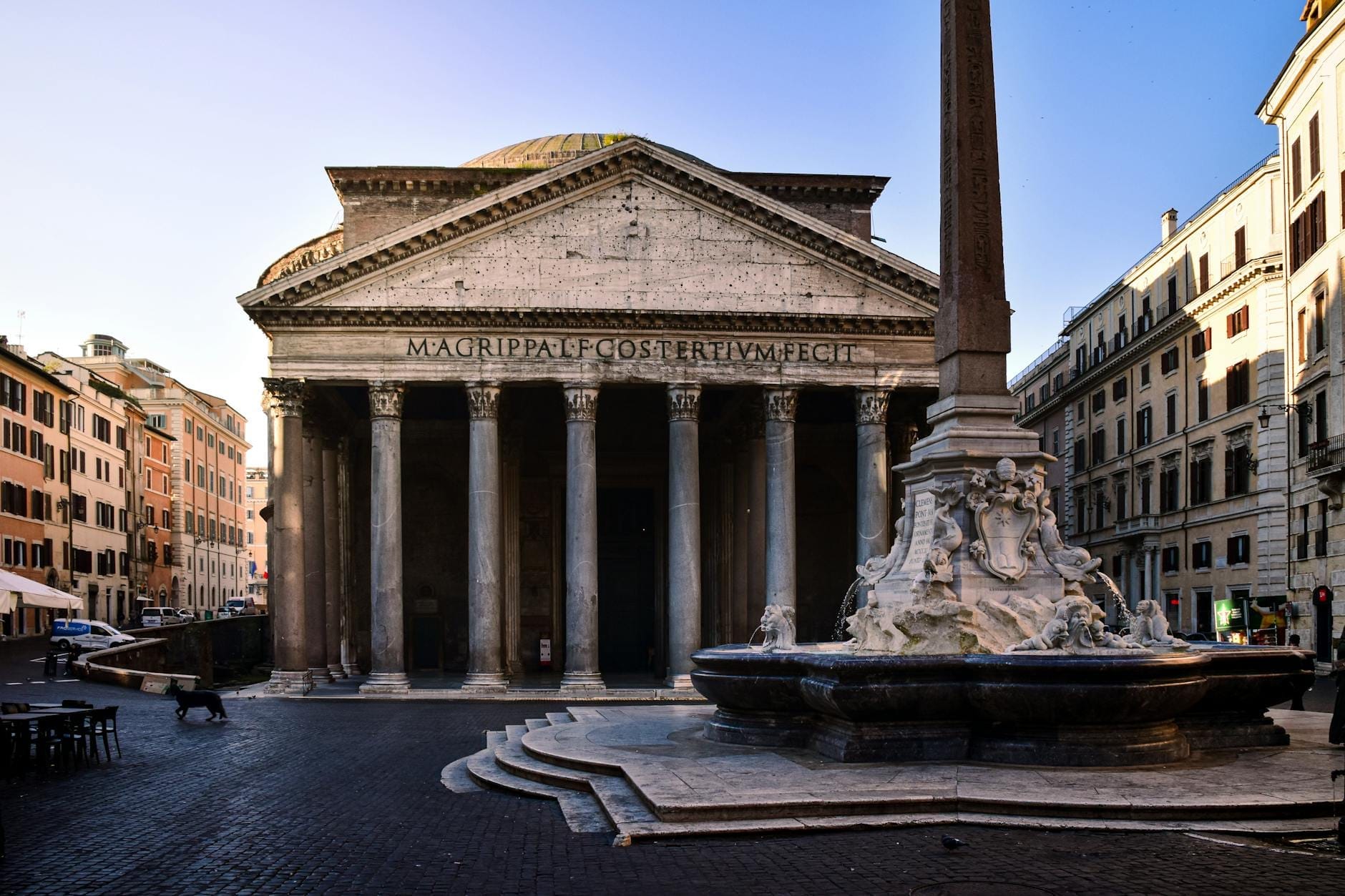 Wide view of the Pantheon with its columns and fountain in front, surrounded by buildings in Rome's historic center.