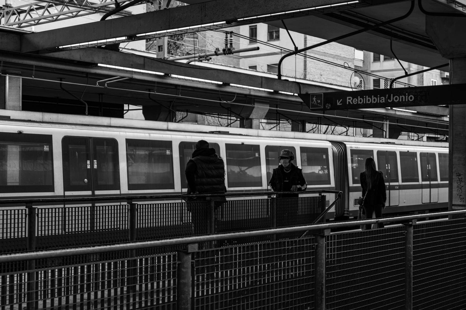 People standing on a Rome metro platform at Rebibbia/Jonio station with a train in the background.
