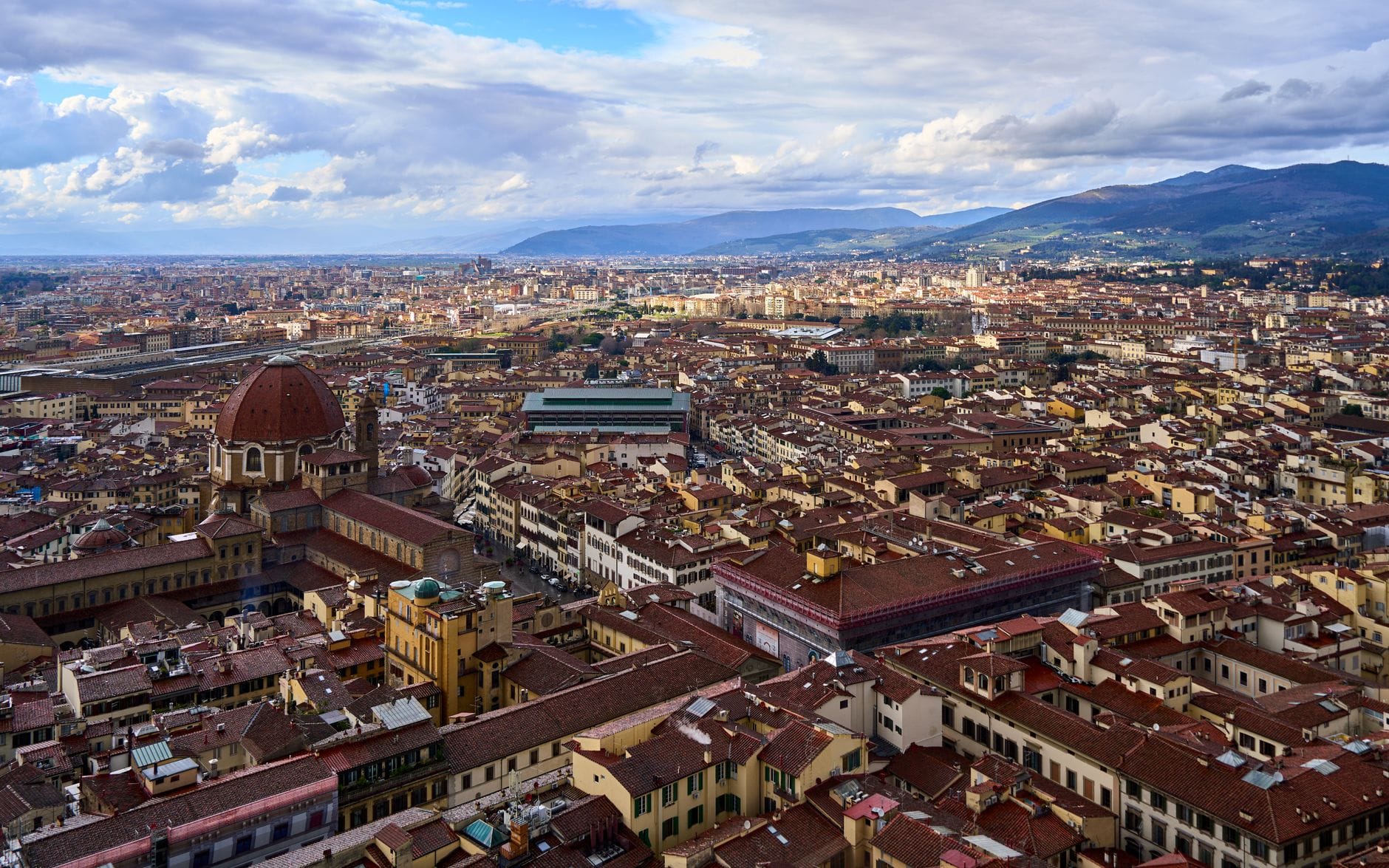 มุมมองทางอากาศของเมืองฟลอเรนซ์พร้อมสถานีรถไฟ Santa Maria Novella และหลังคาบ้านใต้ท้องฟ้ามีเมฆ