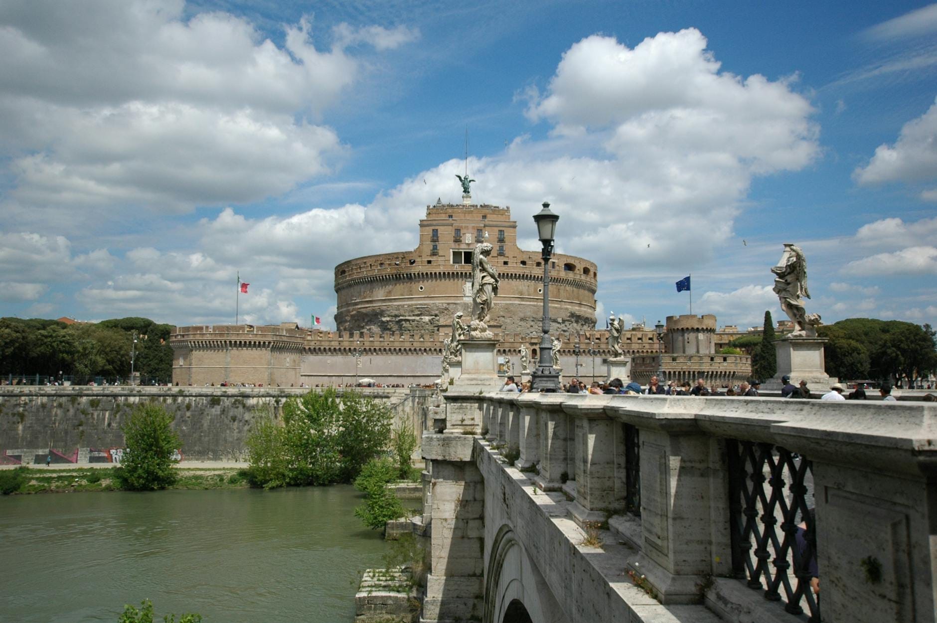 Wide view of Castel Sant'Angelo with the arched bridge and stone statues, popular kid-friendly site in Rome, under a bright blue sky.