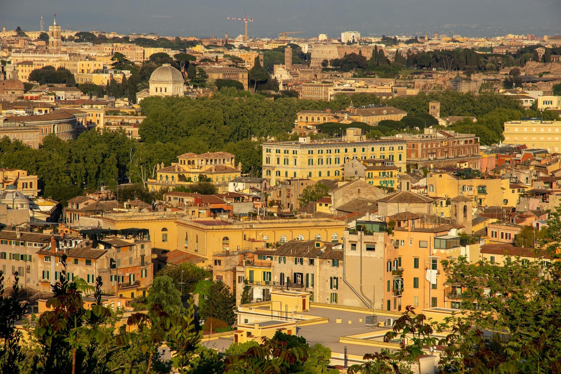 Wide panoramic view of Rome's neighborhoods with classic yellow buildings, domes, and greenery under a clear sky.