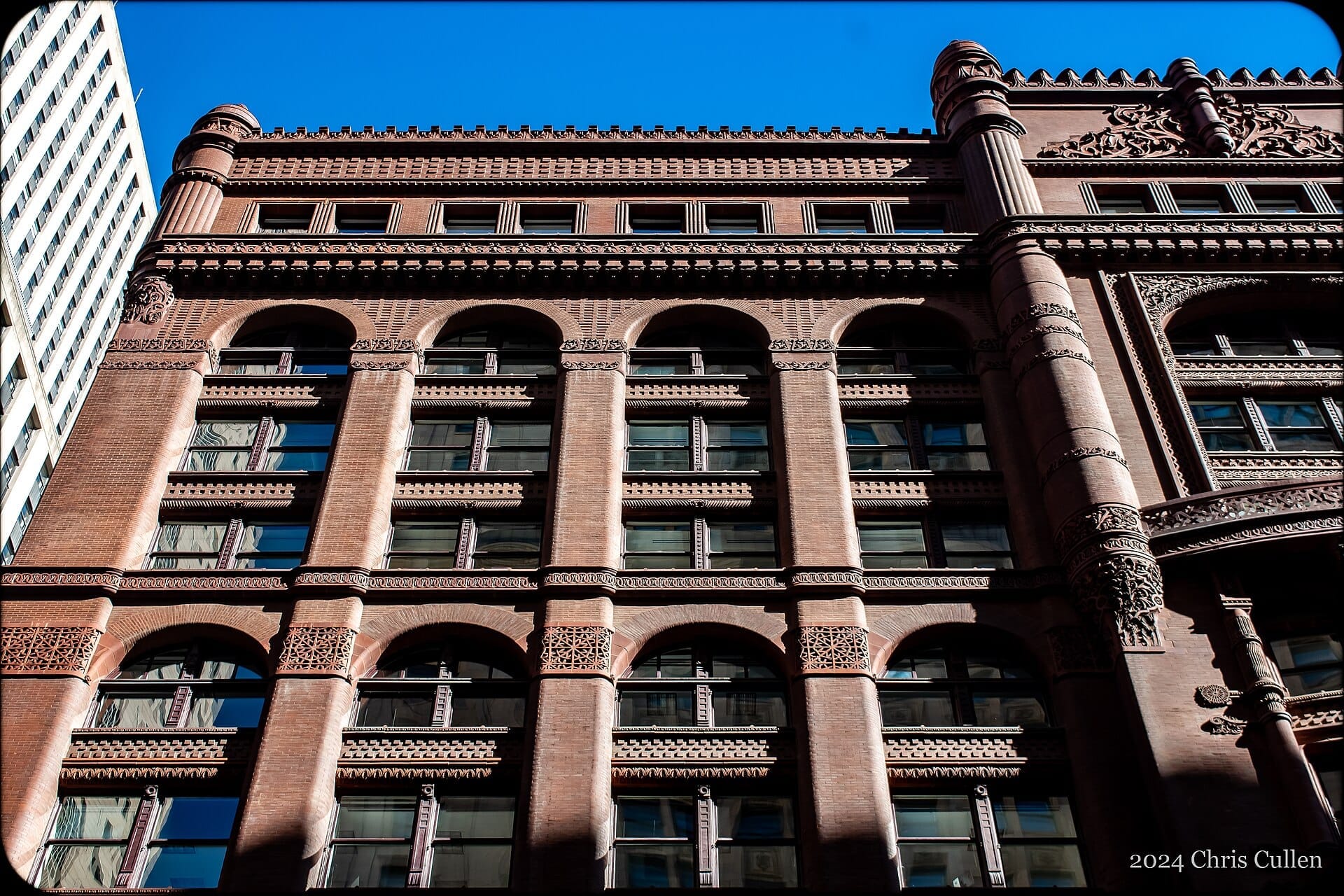 Vista dettagliata della storica facciata in mattoni rossi e degli ornati elementi architettonici del Rookery Building contro un cielo azzurro limpido di Chicago.