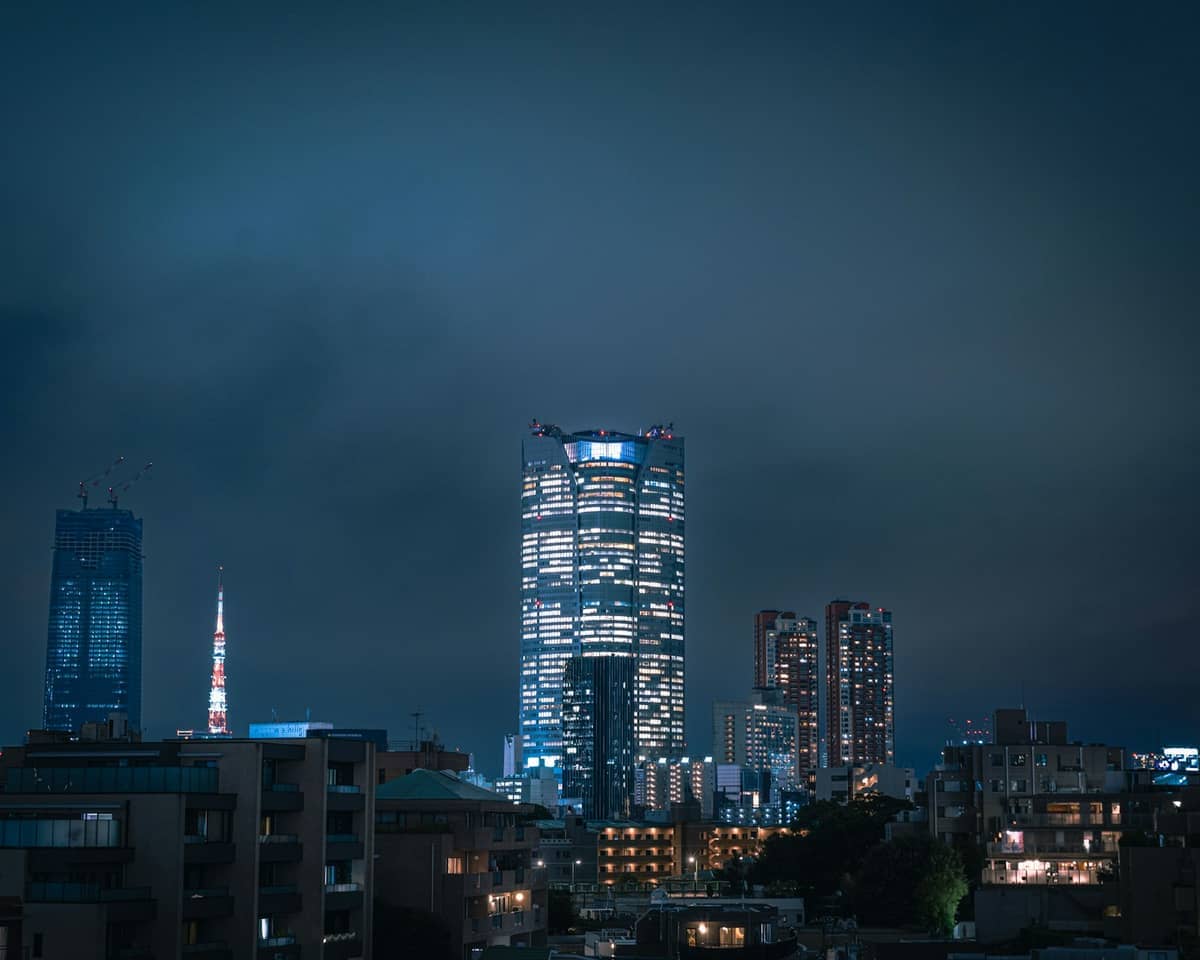 Nighttime cityscape of Roppongi Hills in Tokyo, with illuminated Mori Tower and surrounding modern high-rise buildings under a moody sky.