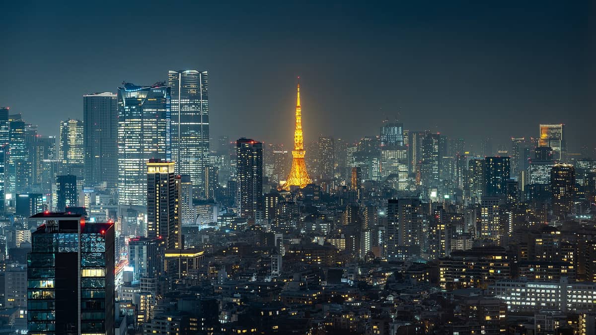 Night skyline of Roppongi featuring Tokyo Tower illuminated in orange, surrounded by modern skyscrapers and city lights.