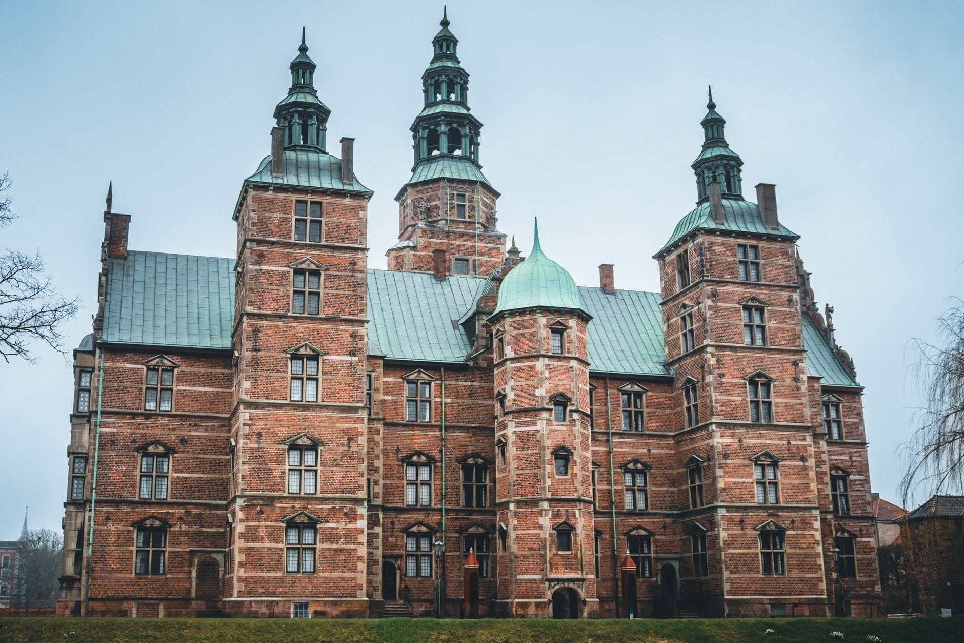 Vista frontale del Castello di Rosenborg a Copenaghen in una giornata nuvolosa, con la sua caratteristica architettura rinascimentale in mattoni rossi e le torri con cupole in rame verde.