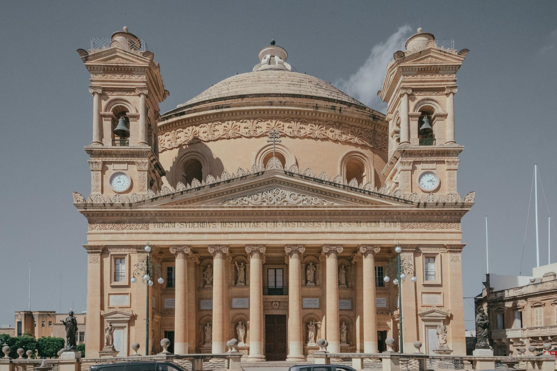 Vista frontale della Rotonda di Mosta con la sua imponente facciata neoclassica, la grande cupola e due campanili sotto un cielo terso.