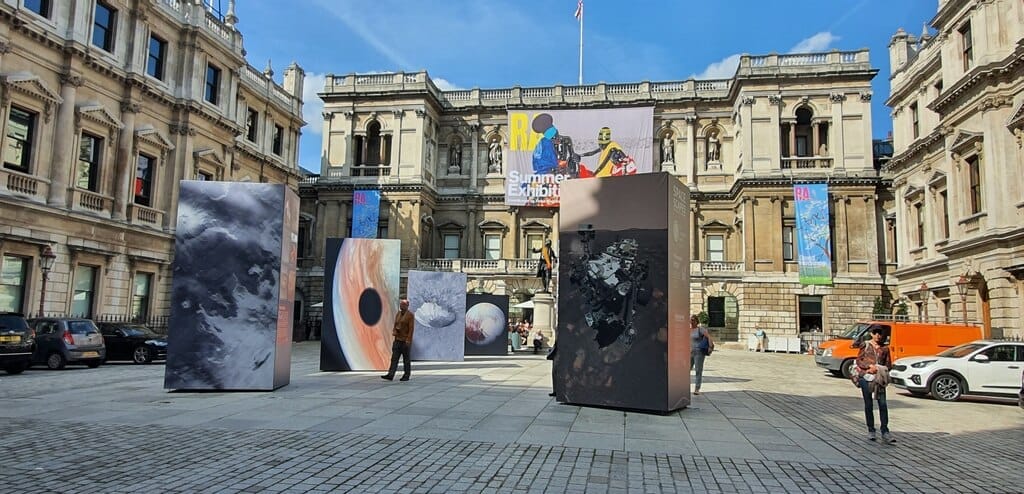 Il cortile della Royal Academy of Arts a Londra con grandi installazioni d'arte contemporanea e architettura palladiana classica sotto un cielo azzurro brillante.
