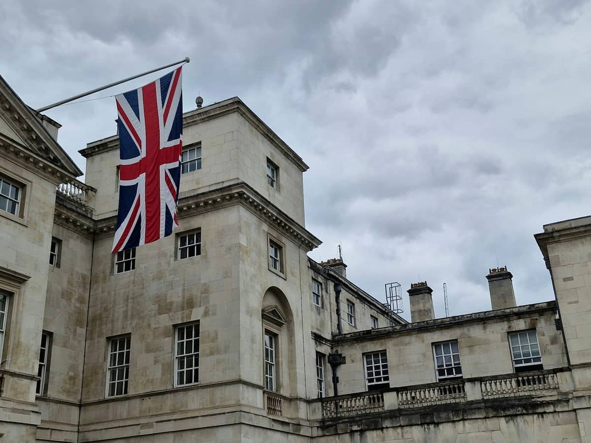 Um imponente edifício de pedra em Londres com uma grande bandeira Union Jack hasteada, evocando o patrimônio britânico e a tradição real.