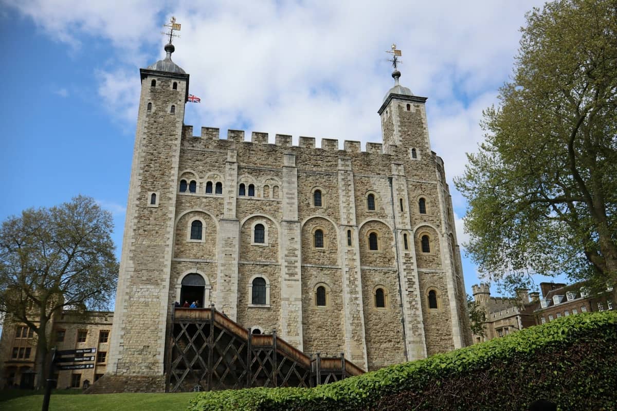 A Torre Branca na Torre de Londres, uma enorme fortaleza medieval de pedra com torres gêmeas, vista em um dia luminoso com céu azul e grama verde.
