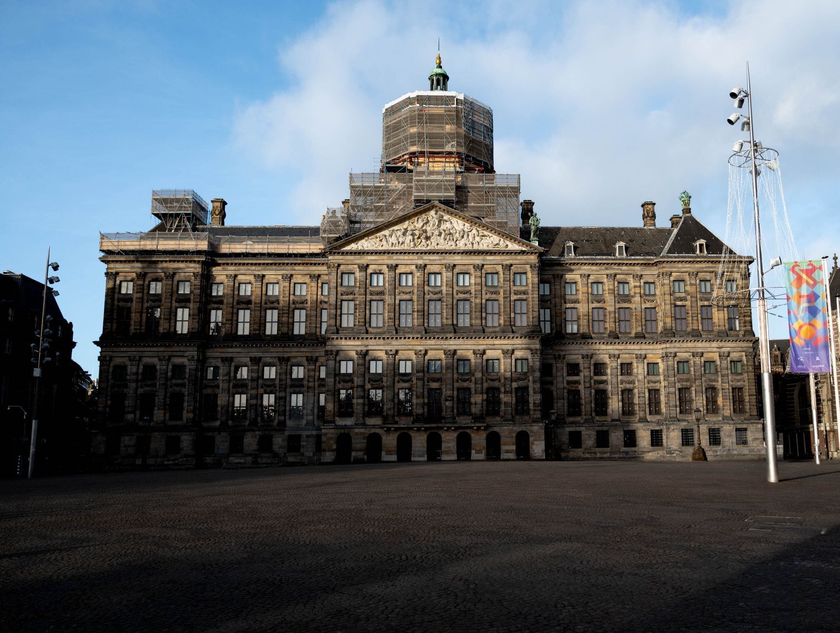 Vista frontal del Palacio Real de Ámsterdam en la Plaza Dam, con su imponente arquitectura del Siglo de Oro neerlandés bajo un cielo luminoso.