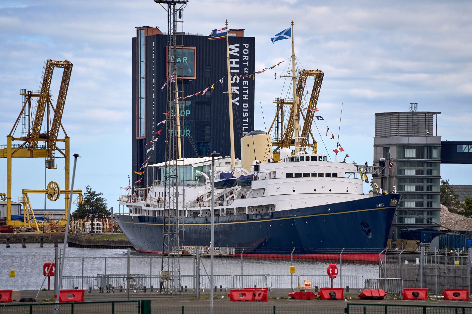 Die Royal Yacht Britannia liegt am Ocean Terminal in Leith vor Anker, mit wehenden Flaggen und Industriestrukturen des Hafens im Hintergrund.
