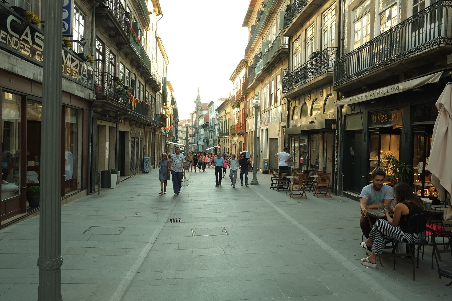 I pedoni passeggiano lungo la Rua das Flores a Porto, fiancheggiata da facciate storiche, balconi in ferro battuto e caffè al piano strada nella calda luce della sera.