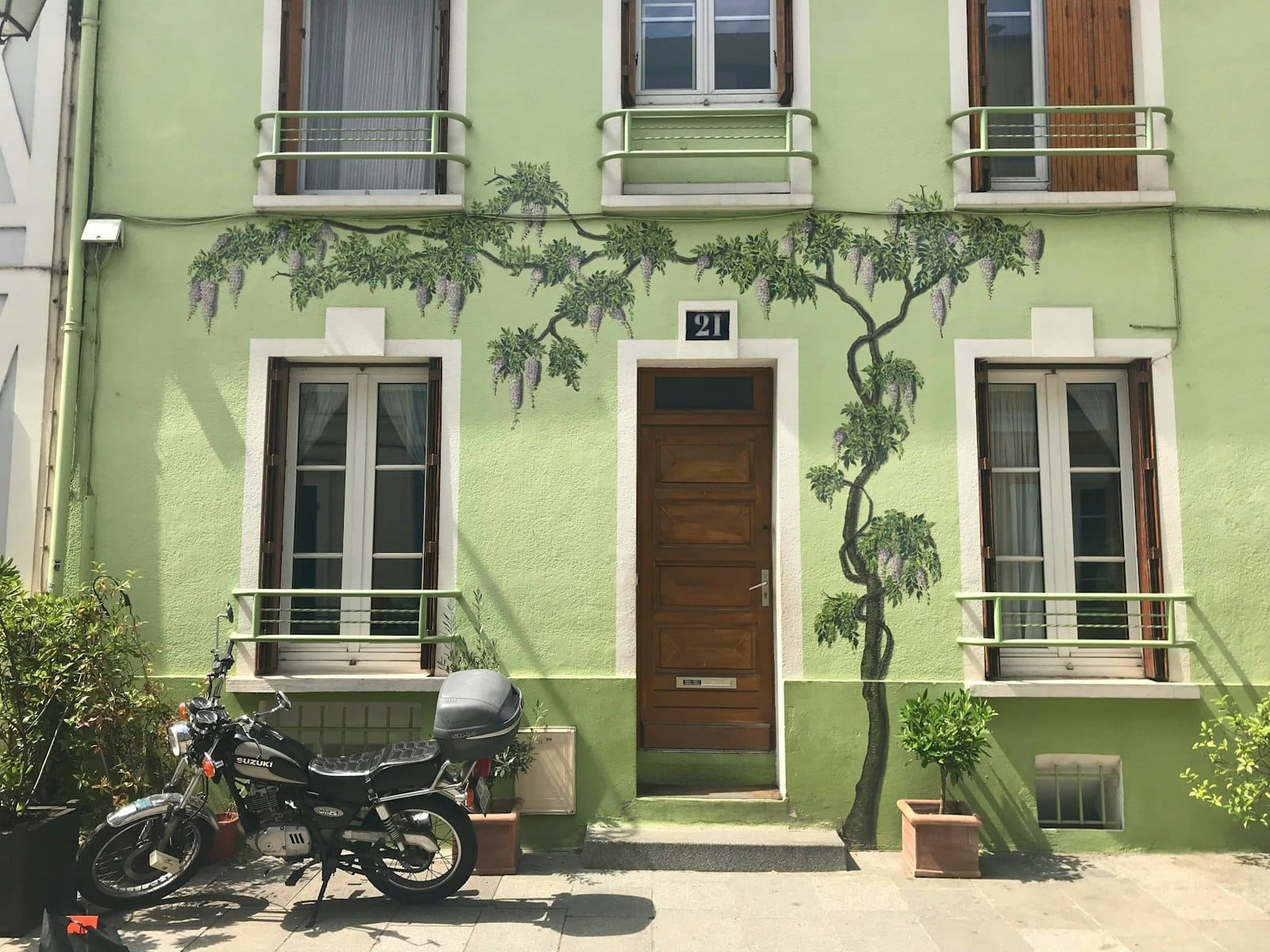 Casa a schiera color verde pastello con glicine dipinto, porta in legno e moto parcheggiata fuori sulla Rue Crémieux, Parigi, in luce naturale.