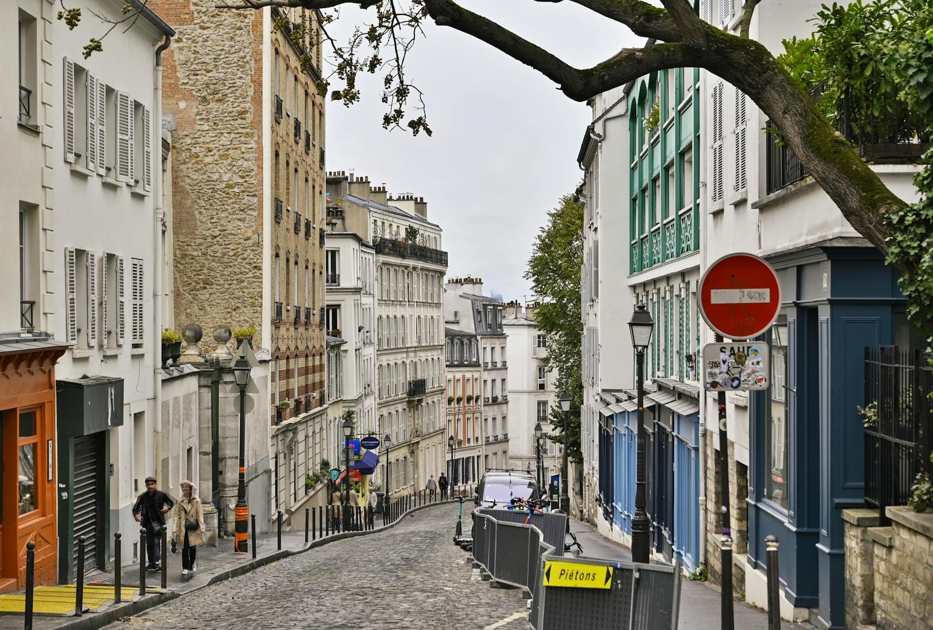 Una strada lastricata dal profilo dolcemente curvo a Parigi, fiancheggiata da edifici classici, negozietti e passanti, che cattura il fascino storico e la vita quotidiana di Rue Mouffetard.