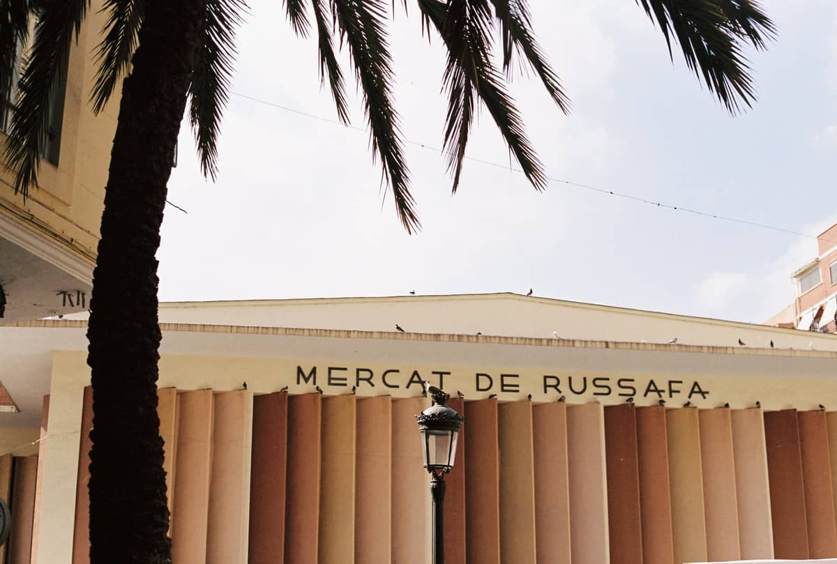 La facciata del Mercat de Russafa, il mercato di quartiere di Ruzafa, Valencia, con le ombre delle palme in primo piano.