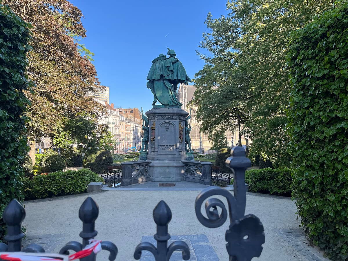 Vista da Place du Grand Sablon em Bruxelas com o monumento de Egmont e Hornes, a praça arborizada e os prédios históricos ao redor em um dia ensolarado.