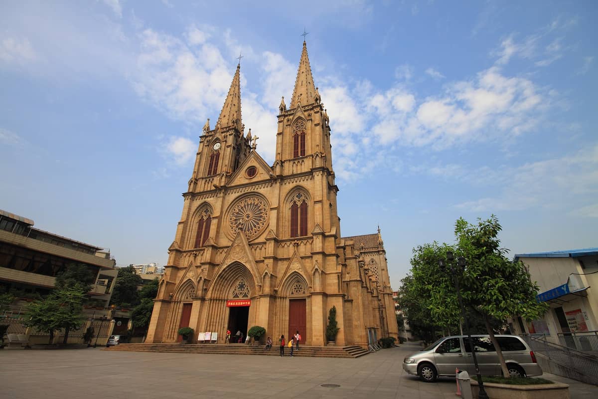 Wide view of the Sacred Heart Cathedral in Guangzhou showing its twin Gothic spires, rose window, ornate granite façade, and main plaza under a blue sky.