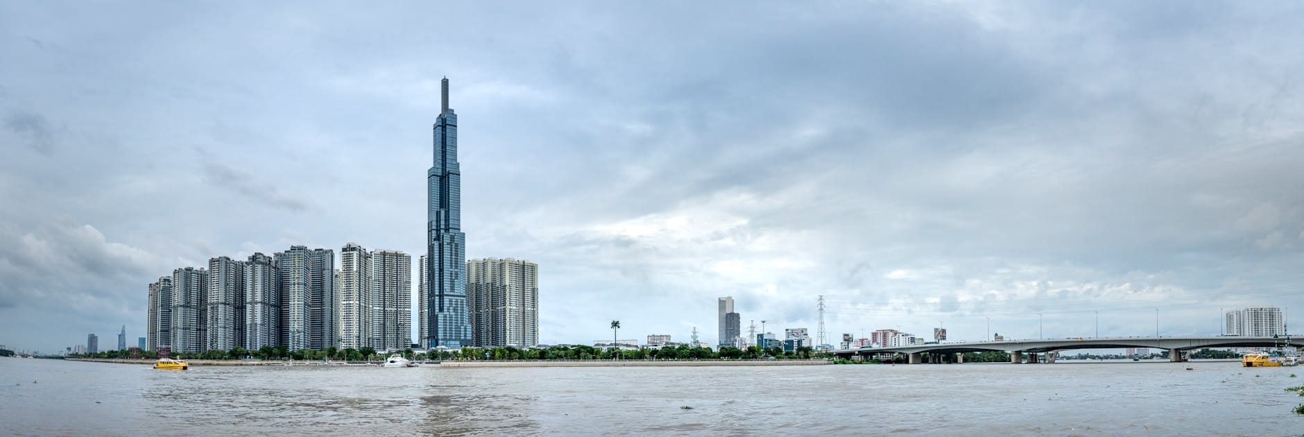 Vista panorámica del río Saigón con modernos rascacielos y la torre Landmark 81 en el horizonte bajo un cielo nublado en Ho Chi Minh City.