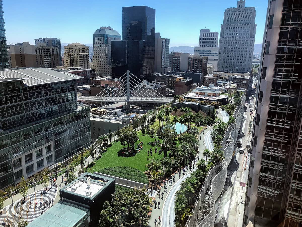 Vista aerea del Salesforce Park che mostra il giardino pensile sopraelevato con sentieri sinuosi, prati, alberi e persone, circondato dagli edifici del centro di San Francisco.