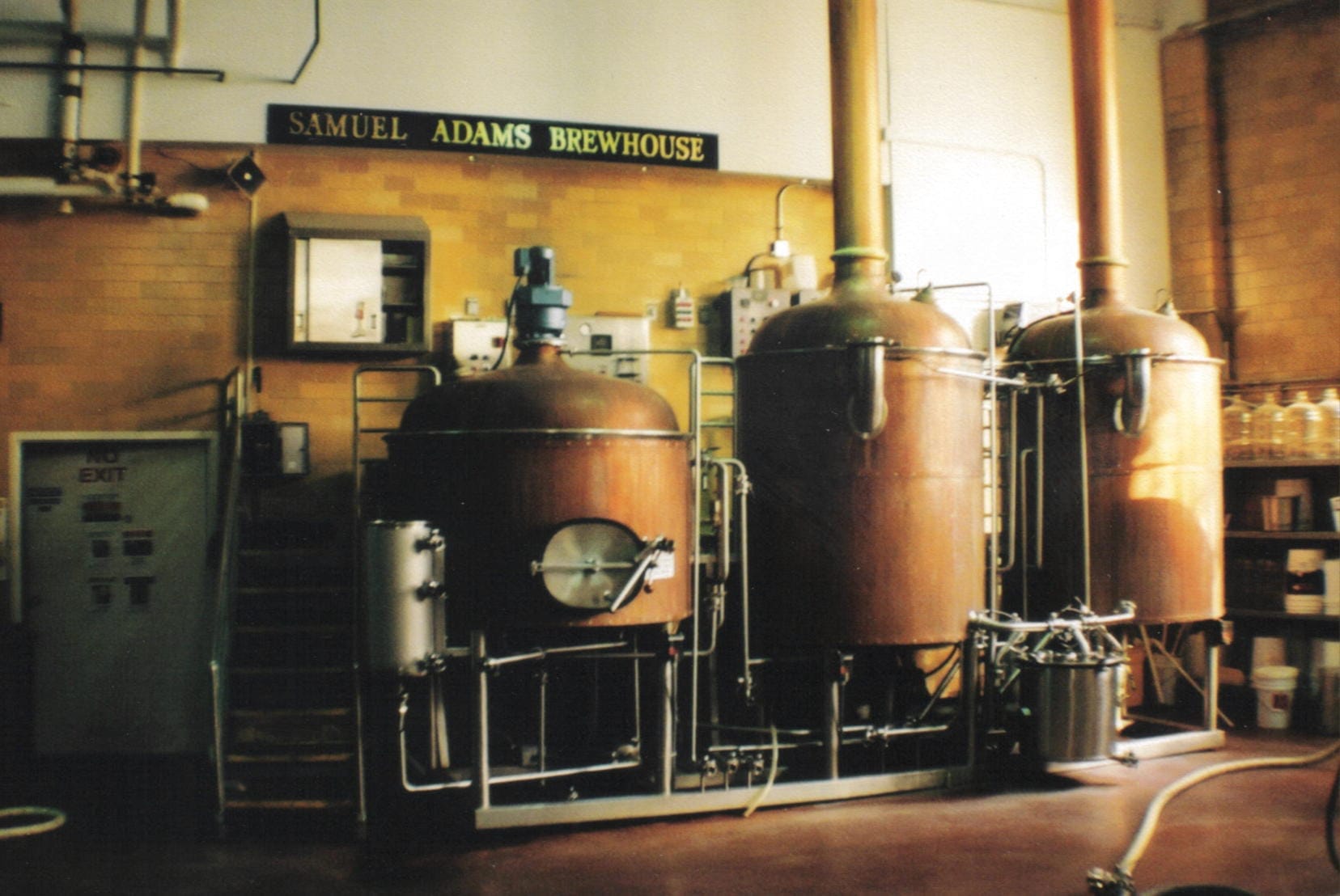 Serbatoi di rame per la produzione di birra e attrezzature industriali all'interno del Samuel Adams Brewhouse, con pareti di mattoni gialli e illuminazione naturale soffusa.