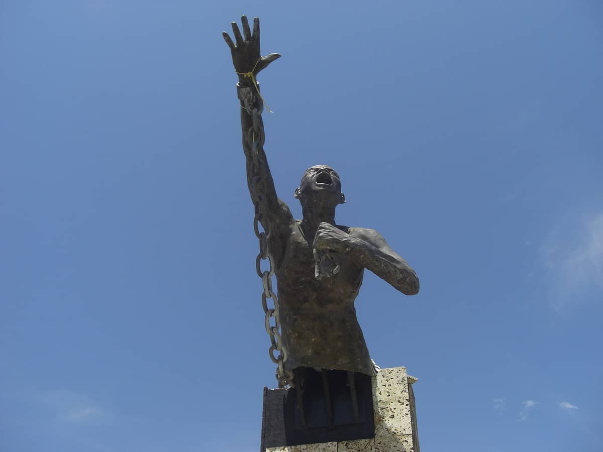 Bronze statue of a man breaking free from chains against a clear blue sky in San Basilio de Palenque, Colombia.