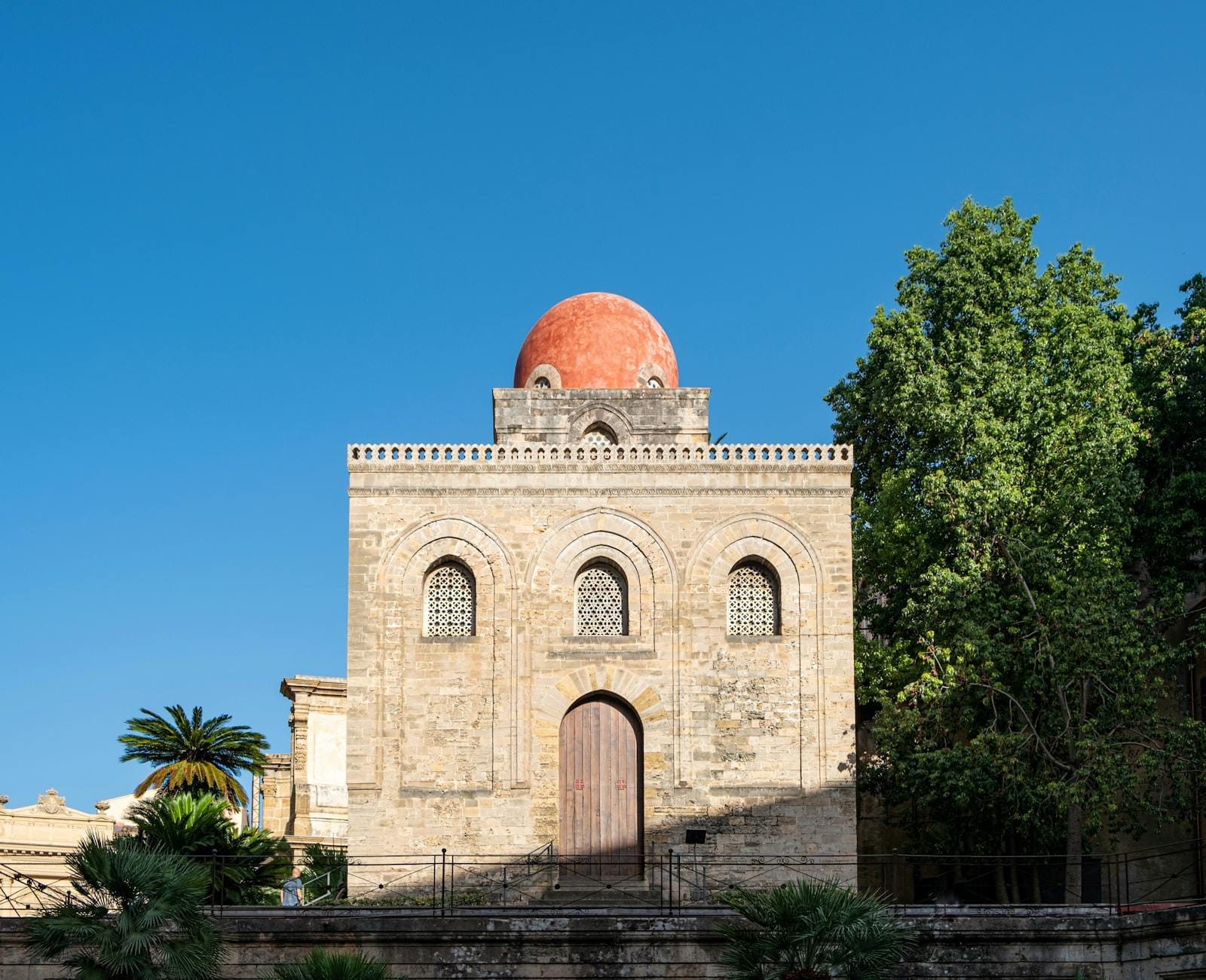 Frontansicht der Kirche San Cataldo in Palermo mit steinerner Fassade und einer charakteristischen roten Kuppel unter klarem blauen Himmel.
