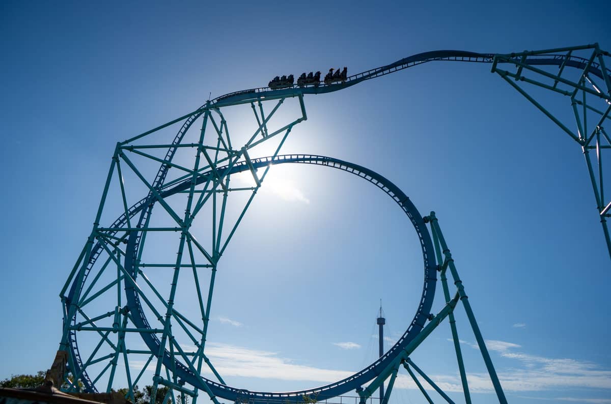Eine große Stahlachterbahn mit Fahrgästen, die hoch gegen einen blauen Himmel in einem Freizeitpark in San Diego schleift.