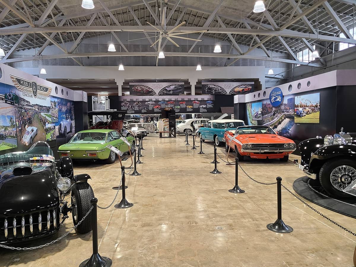 รถยนต์คลาสสิกที่จัดแสดงใต้เพดานโค้งสูงในห้องจัดนิทรรศการของ San Diego Automotive Museum ที่ Balboa Park พร้อมไฟสปอตไลท์หลากสีสันและกราฟิกบนผนังที่ให้ข้อมูล