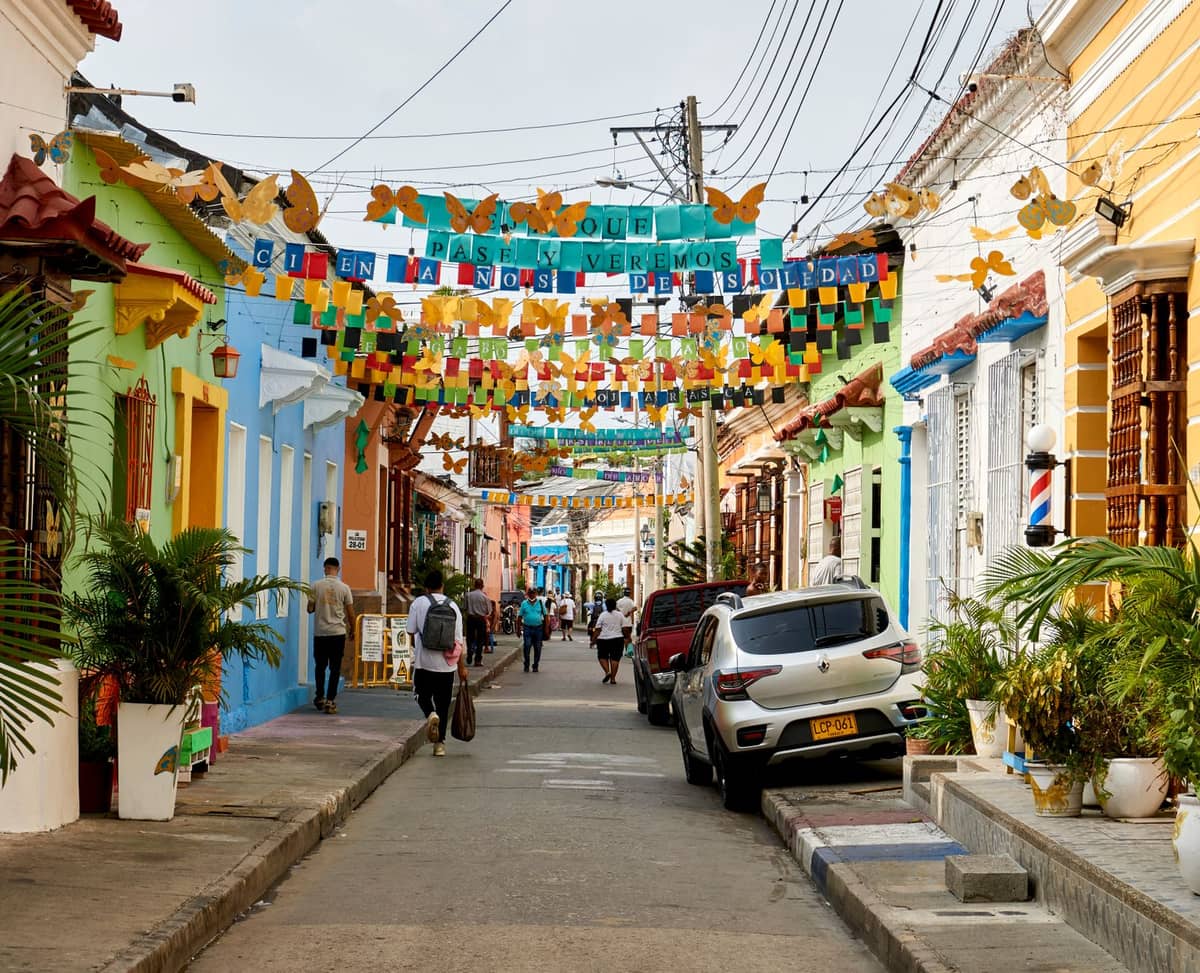 Colorful colonial street in the San Diego neighborhood of Cartagena, with people walking, festive decorations, and charming facades under a bright sky.