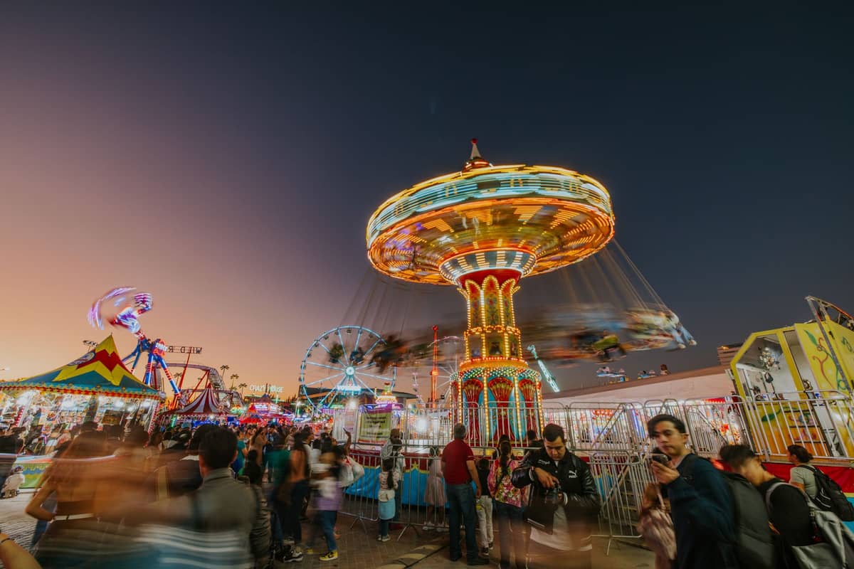 Abendliches Gedränge auf einem hell erleuchteten Jahrmarkt mit Fahrgeschäften, Riesenrad und Besuchern, die die lebhafte Atmosphäre der San Diego County Fair genießen.