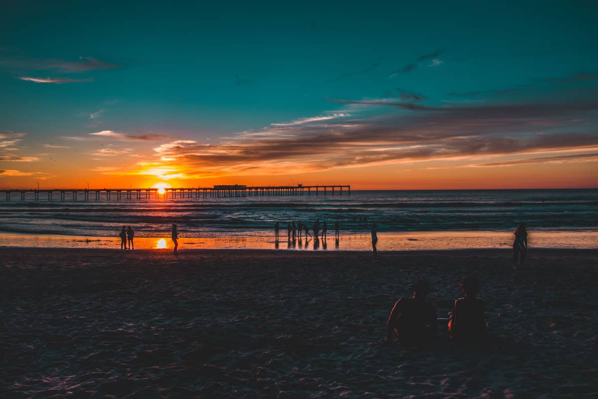 Paare und Besucher beobachten einen farbenprächtigen Sonnenuntergang über dem Ozean vom Strand am Ocean Beach Pier in San Diego, Kalifornien.