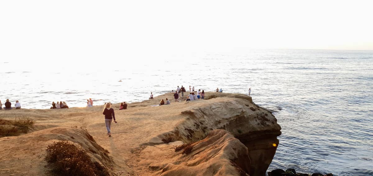 Menschen sitzen und spazieren auf dramatischen Sandsteinklippen mit Blick auf den Pazifischen Ozean bei Sonnenuntergang, mit brechenden Wellen darunter an den Sunset Cliffs in San Diego.