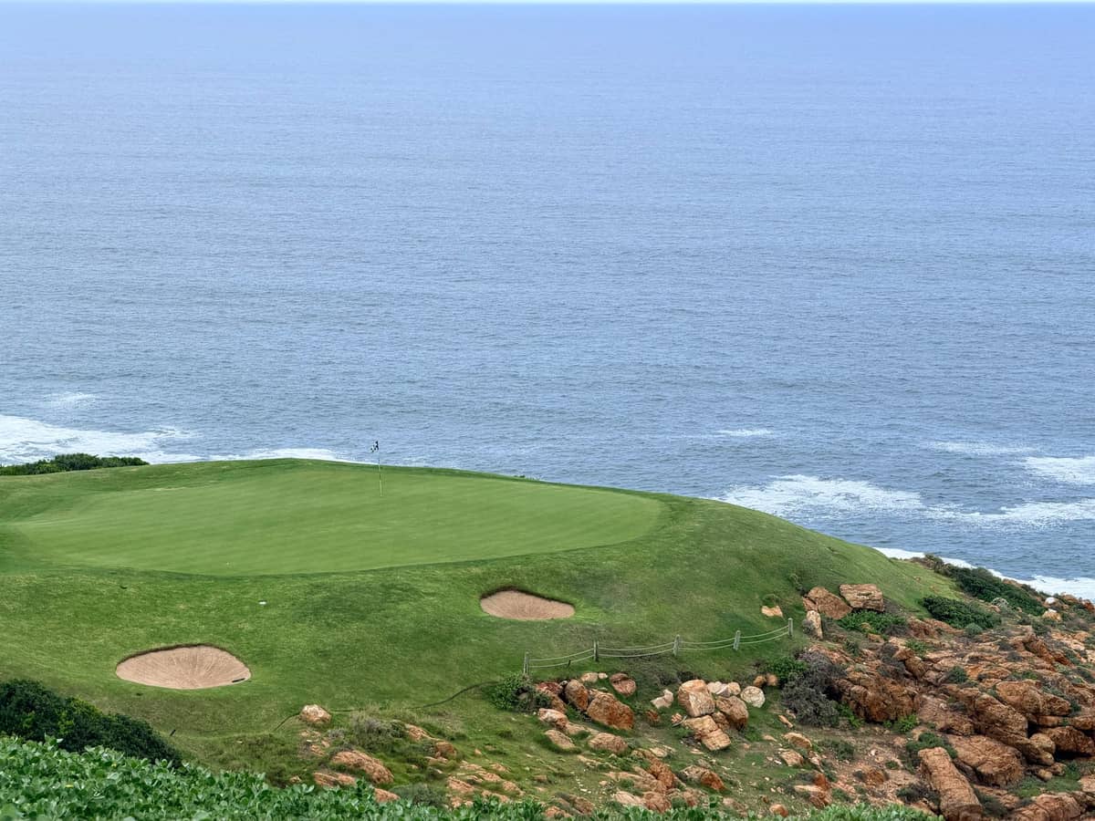 Golfgrün und Bunker auf einer Klippe mit Blick auf den Ozean, darunter felsige Küste und Wellen.
