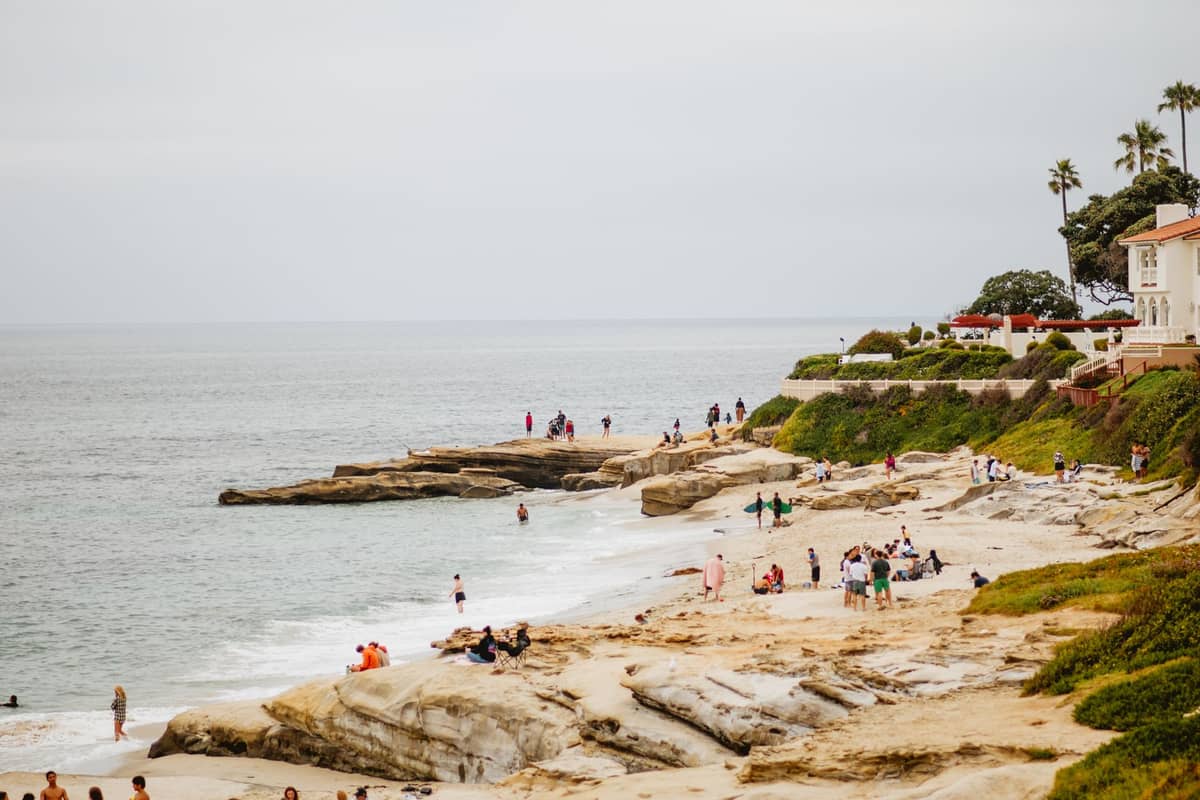 Menschen, die bei bewölktem Himmel an La Jollas felsiger Küste spazieren und entspannen, als Beispiel für San Diegos mildes Strandwetter im Winter.