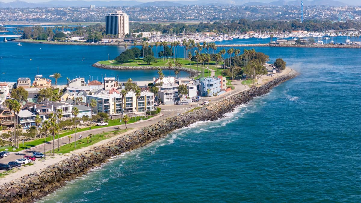 Luftaufnahme von Gebäuden und Resorts in San Diego entlang einer felsigen Küste mit ruhigem Buchtgewässer und einem sichtbaren Jachthafen im Hintergrund.
