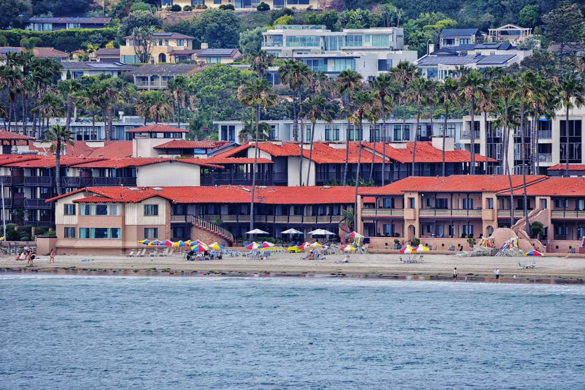 Strandresortgebäude mit roten Ziegeldächern, Sonnenschirmen und Palmen entlang des Sandes in San Diego.