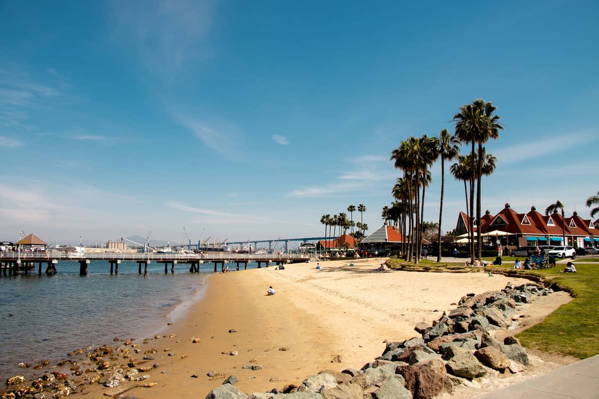 Ein Sandstrand mit Palmen, einer felsigen Küstenlinie, Piers und Strandresortgebäuden in San Diego unter einem klaren blauen Himmel.