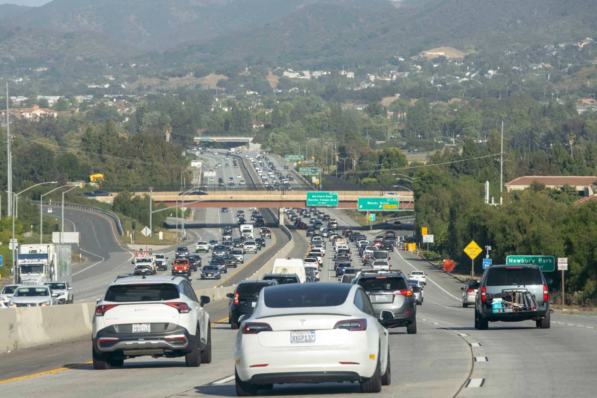 Dichter Verkehr auf einem Freeway in Kalifornien mit grünen Hinweisschildern, Autos und Hügeln im Hintergrund, aufgenommen von hinter den Fahrzeugen.