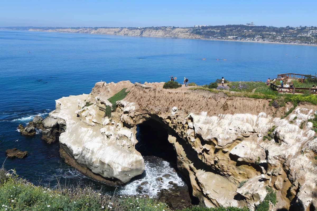 Malerischer Blick auf die zerklüftete Küste von La Jolla mit einer beeindruckenden Meereshöhle, Klippen und Spaziergängern oben, mit Blick auf die blauen Gewässer des Pazifiks.