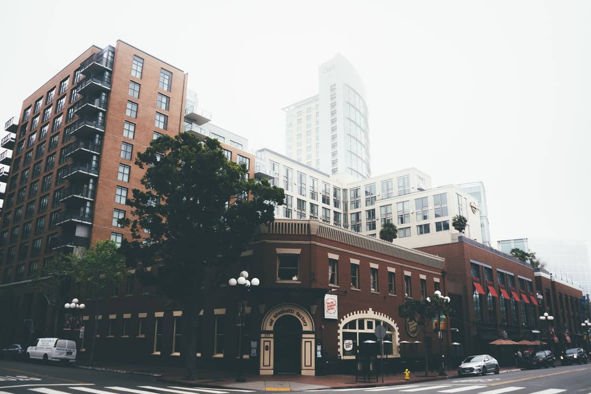 Straßenecke im Gaslamp Quarter von San Diego mit einem historischen Backsteingebäude, Laternenmasten und modernen mittelhohen Gebäuden im Hintergrund.