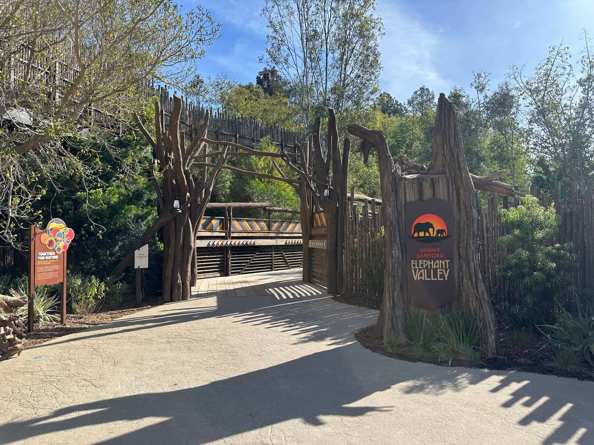 Eingang zum Elephant Valley im San Diego Zoo mit Holztoren, thematischer Beschilderung und üppigem Grün unter einem klaren Himmel.