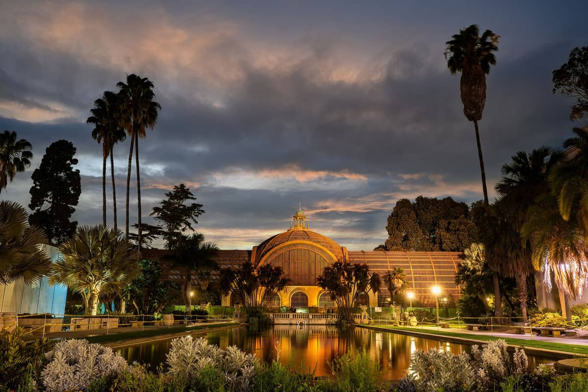 Dämmerungsansicht des ikonischen Botanical Building im Balboa Park mit Spiegelteich, Palmen und üppiger Bepflanzung in San Diego.