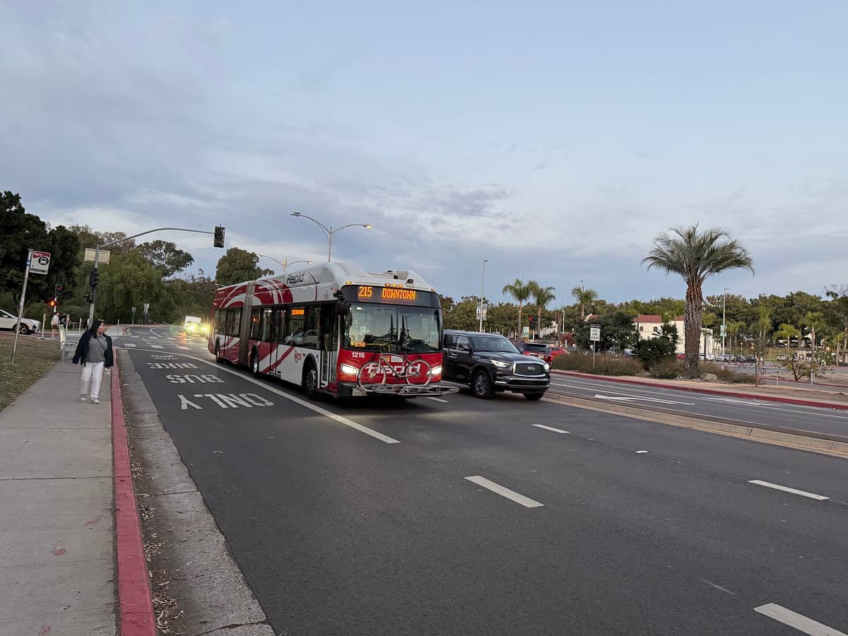 San Diego MTS Rapid-Bus an einer Haltestelle in der Nähe des Balboa Park mit Palmen und einem Parkplatz im Hintergrund.
