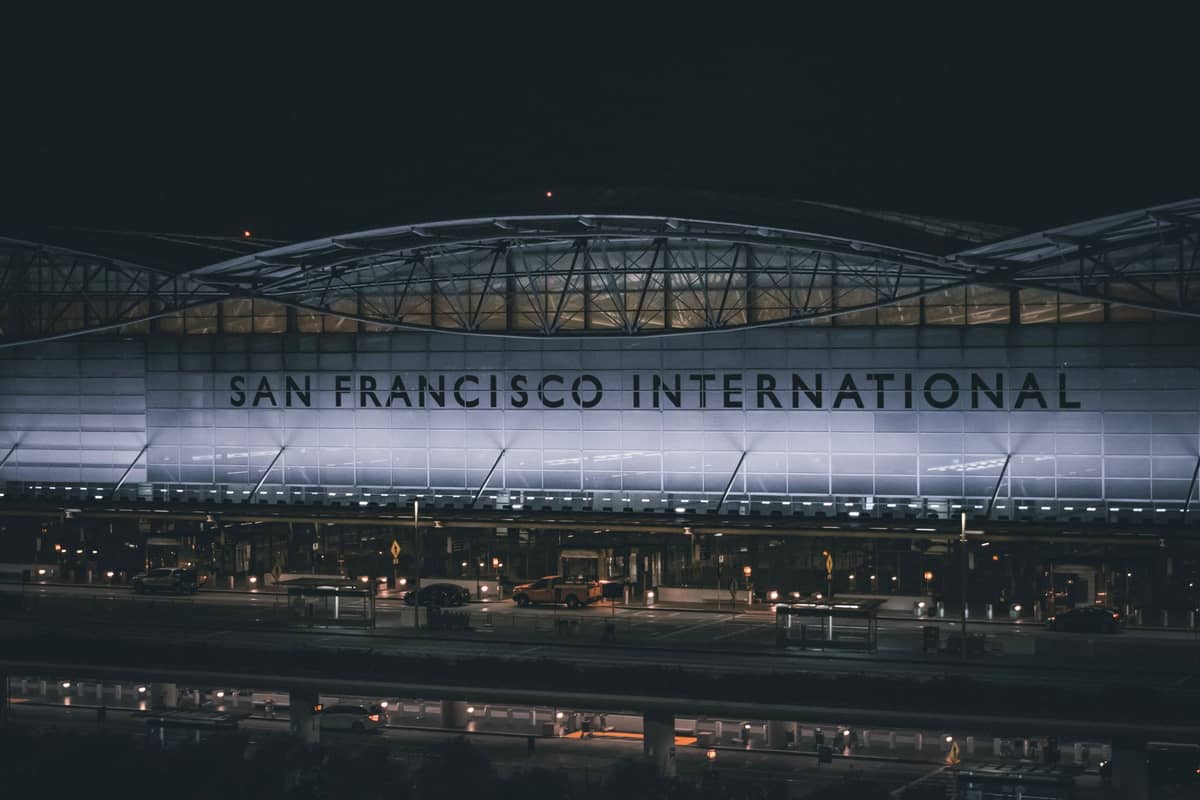 Vista nocturna de la entrada exterior del Aeropuerto Internacional de San Francisco, con su gran letrero iluminado y la zona de bajada de pasajeros.