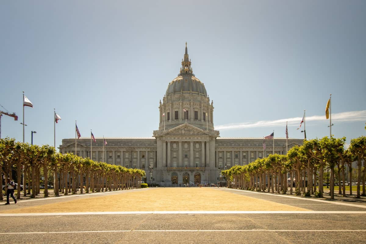 Vista panorámica del Ayuntamiento de San Francisco en un día luminoso, con su gran cúpula, la arquitectura Beaux-Arts de perfecta simetría y un paseo arbolado en primer plano.