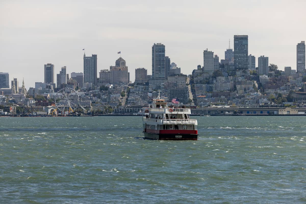 Ferri en la Bahía de San Francisco acercándose al muelle, con el skyline de la ciudad y los embarcaderos de fondo en un día nublado.