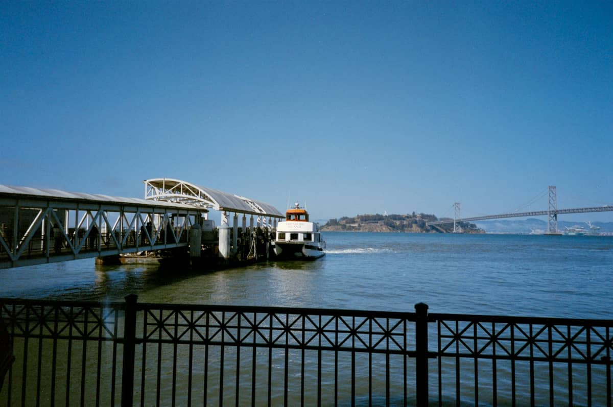 Prom na zatoce San Francisco zacumowany przy nowoczesnym terminalu z mostem Bay Bridge i wyspą Yerba Buena widocznymi w tle.